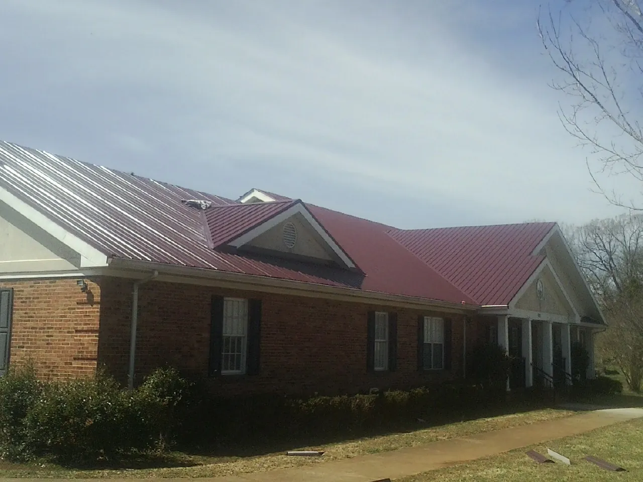 Red metal roof with gabled entries on a long brick building, from a Hail Damage Roof Repair job in Pompeys Pillar