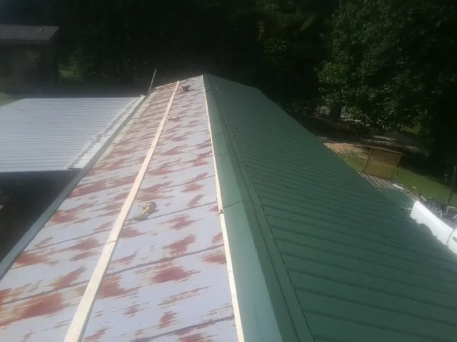 Old rusted panels beside newly installed green metal roofing — Wind Damage Roof Repair by Roofing Brothers in Pompeys Pillar