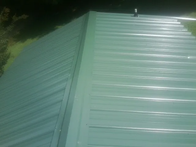 New green metal panels meeting at the ridge of a roof — Flat Roof Repair work by our crew in Pompeys Pillar