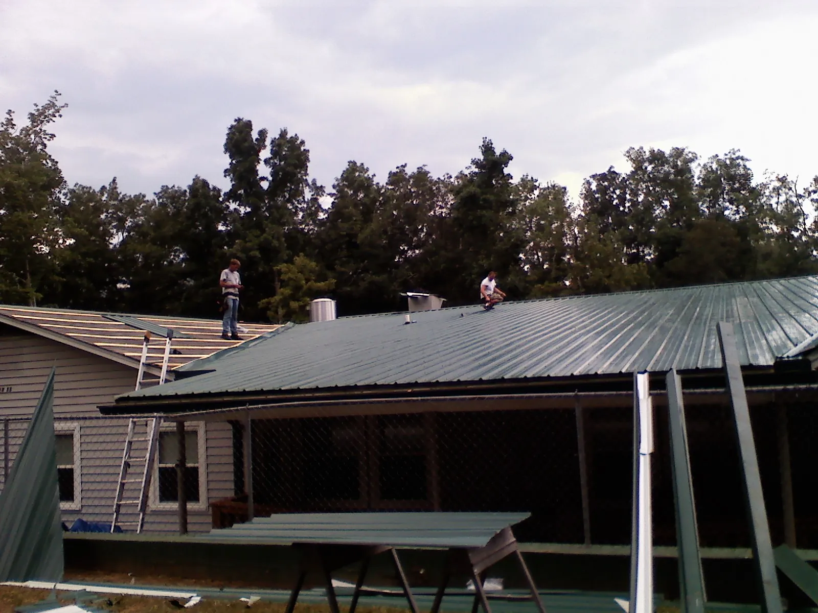 Two roofers installing green metal panels above a covered porch in Pompeys Pillar