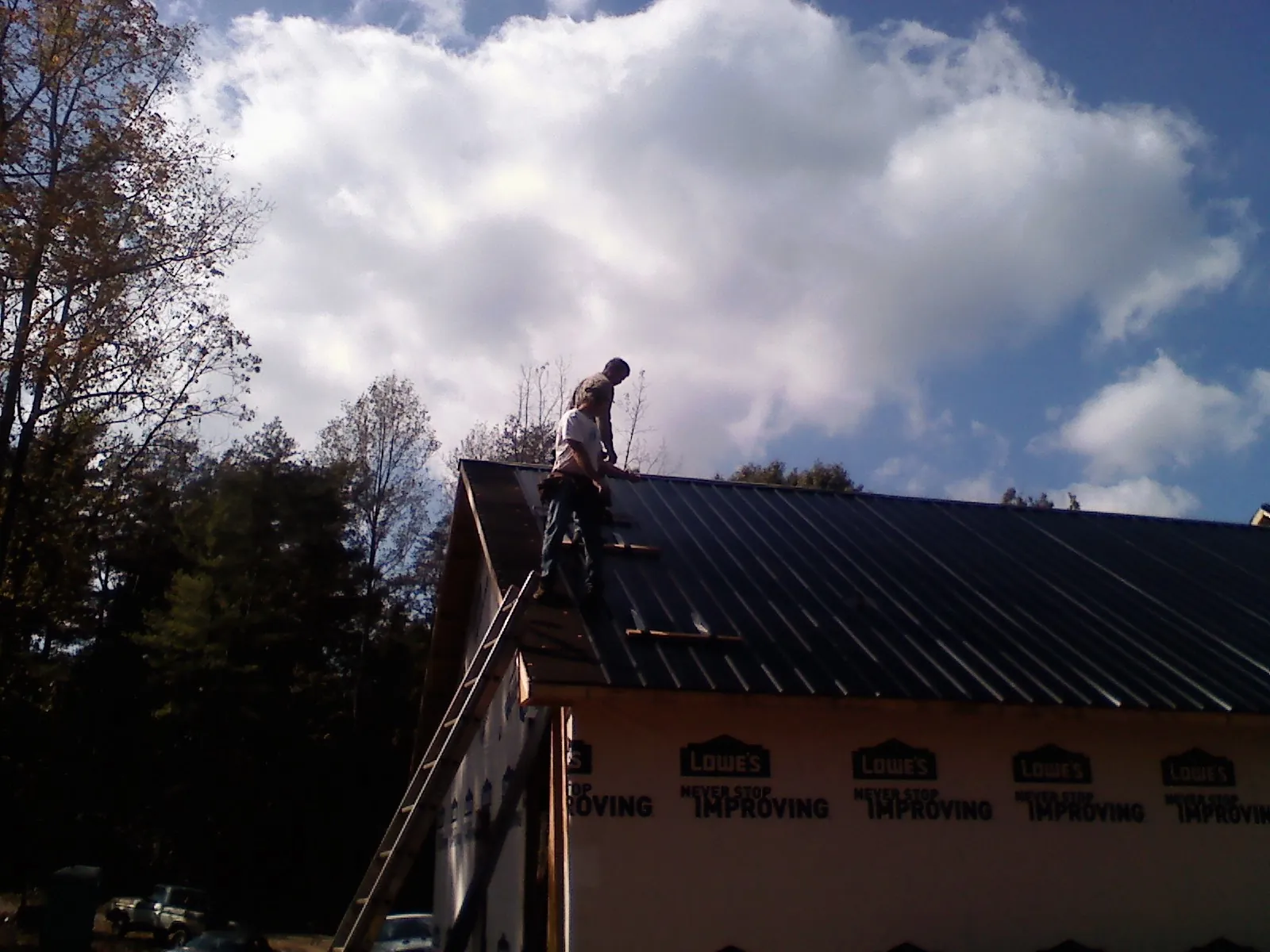 Roofer fastening dark metal panels high against a cloudy sky, from a Roof Inspection job in Pompeys Pillar