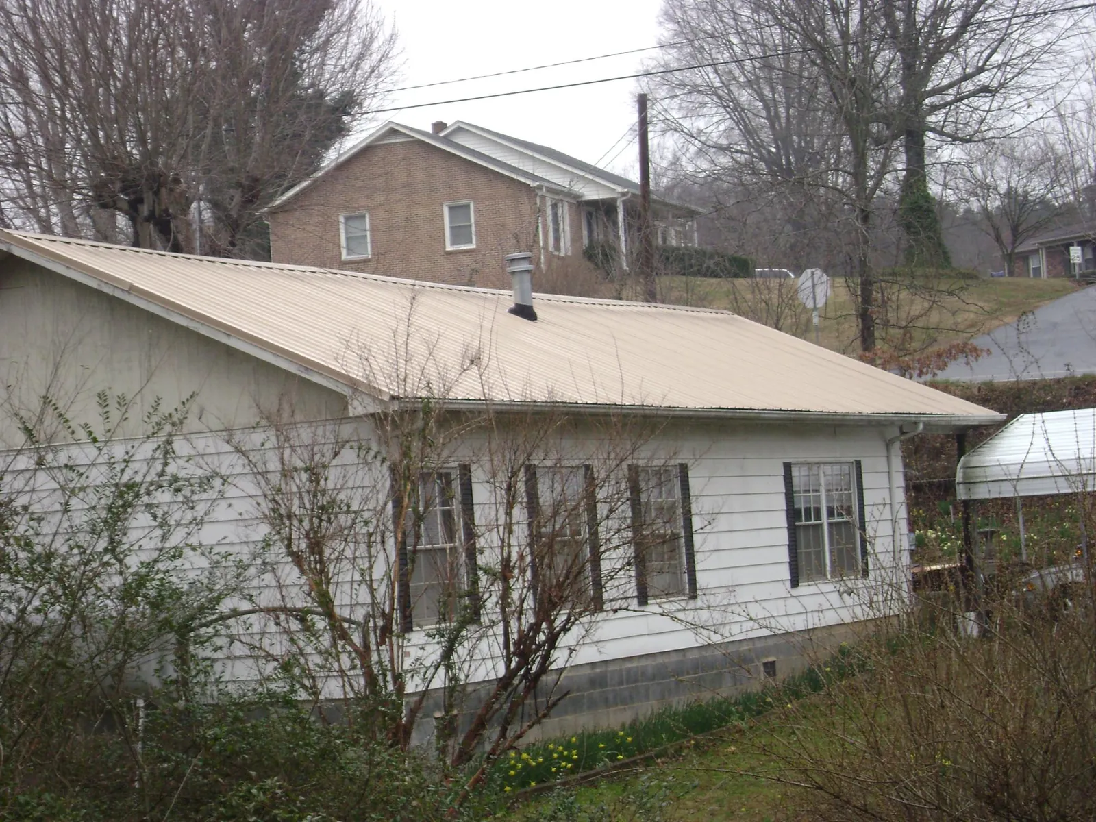 Tan metal roof on a white sided house set into a hillside — Commercial Roofing by Roofing Brothers in Pompeys Pillar